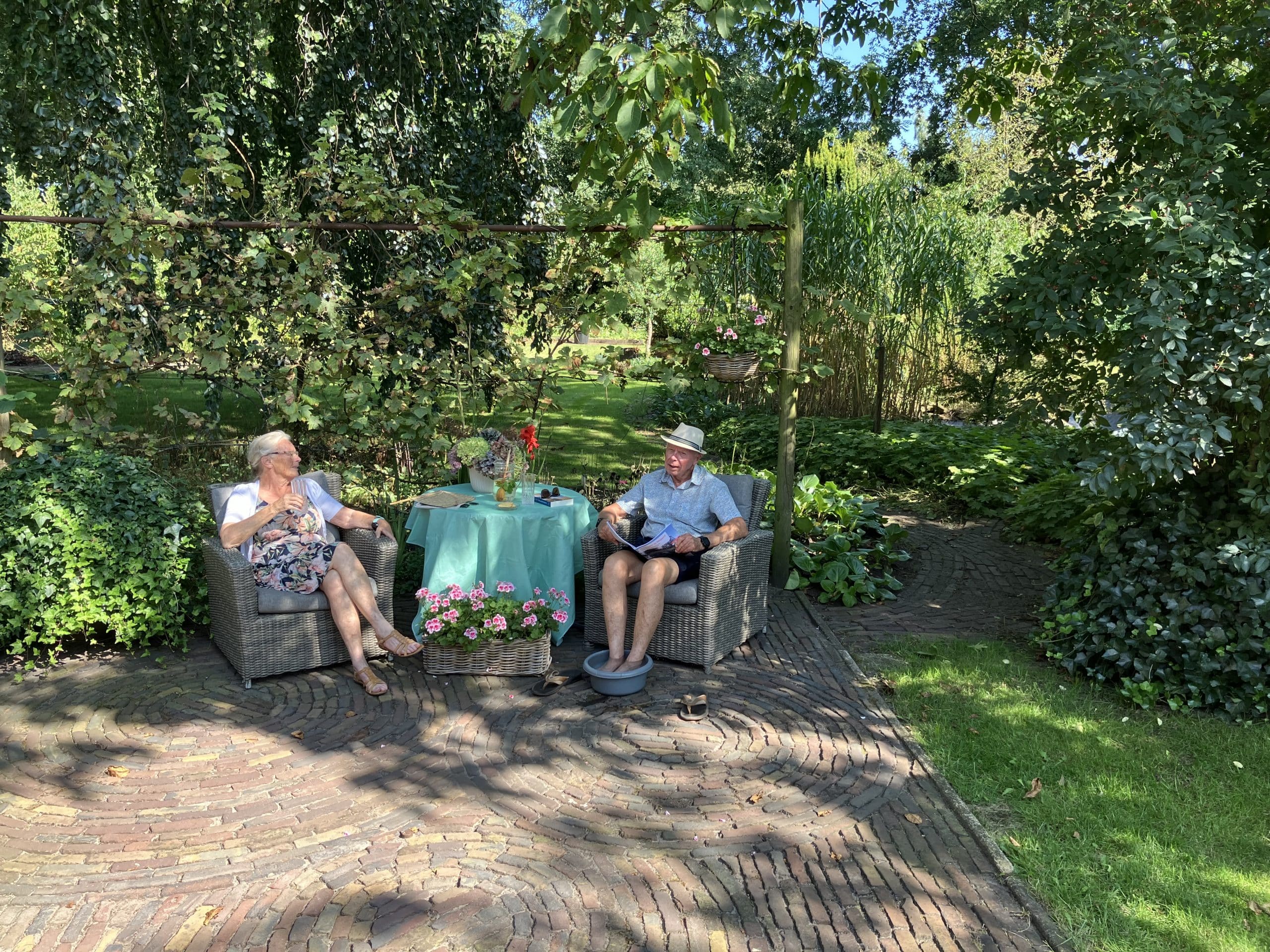 Ouder echtpaar dat in de schaduw zit, de man heeft zijn voeten in een teiltje water tegen de hitte