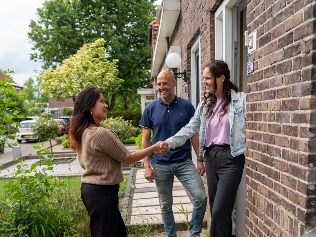 Iemand die bij inwoners thuis komt kijken tijdens de Nationale Duurzame Huizenroute. Ze staan bij de voordeur en geven elkaar een hand