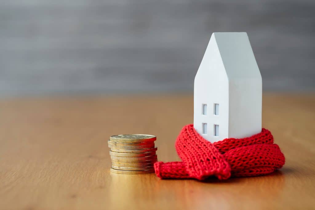 Een klein houten huisje met een sjaal om waar een stapeltje euro's naast ligt