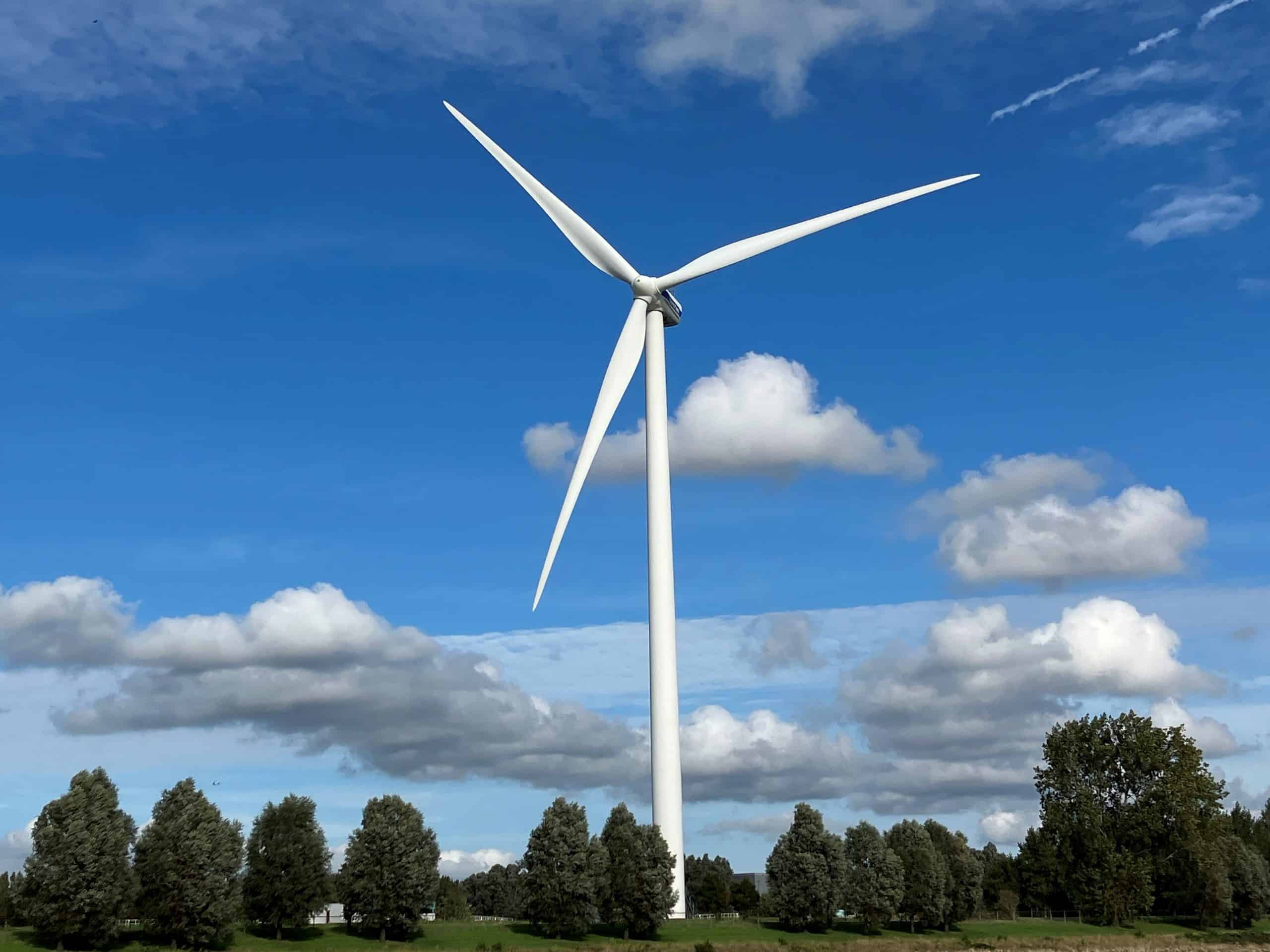 Windmolen tegen een blauwe lucht met wolken en bomen