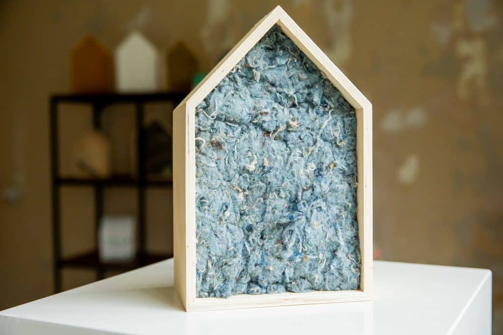 Klein houten huisje op een tafel, gevuld met isolatiemateriaal