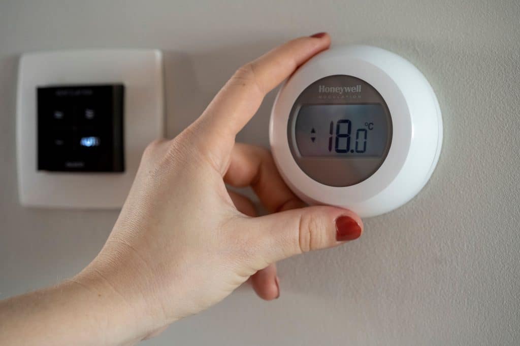 Hand bij een thermostaat die de temperatuur op 18 graden zet